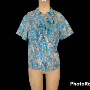 Puede incluir: Una blusa de manga corta con estampado floral azul y verde, cuello con volantes y cierre de botones.