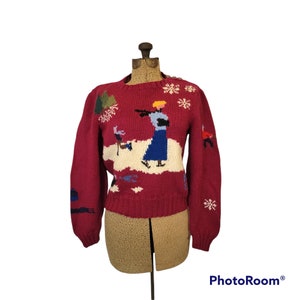 May include: A red knitted sweater with a winter scene featuring a woman and a child ice skating. The scene is embroidered in colorful yarn.