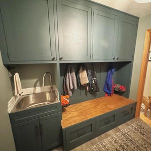 May include: A built-in mudroom unit with dark teal cabinets and a wooden bench. It features a stainless steel sink, storage drawers, and hooks for hanging coats and bags. A dog stands in the doorway.