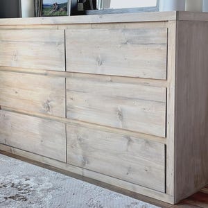 Könnte beinhalten: Eine hellfarbene Holzkommode mit sechs Schubladen. Die Kommode hat eine rechteckige Form und besteht aus hellfarbenem Holz mit sichtbarer Holzmaserung. Die Schubladen sind in zwei Spalten zu je drei angeordnet.