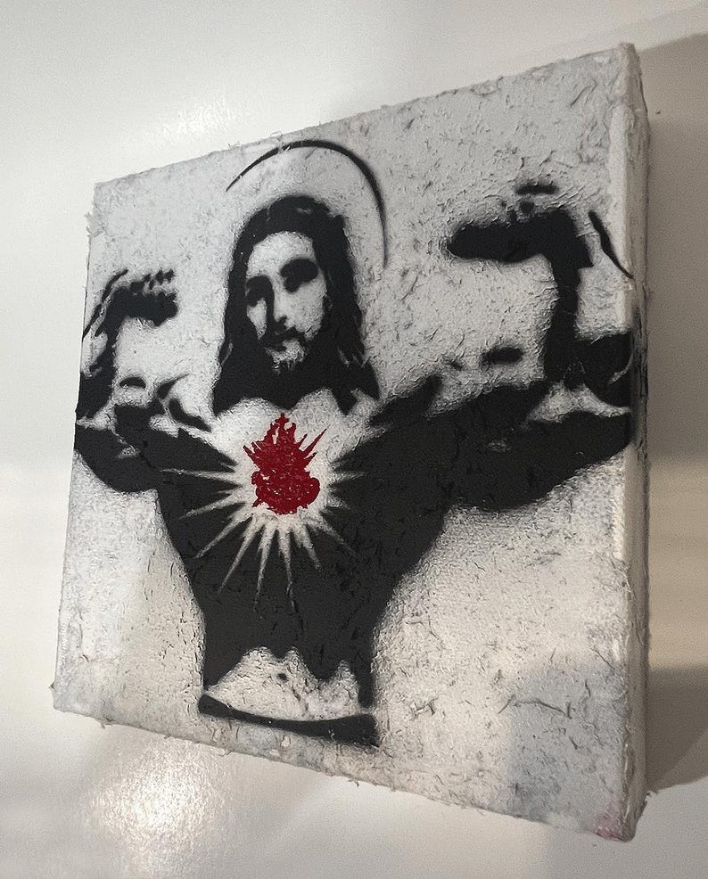 May include: A square canvas art piece featuring a black stencil of Jesus flexing his arms. A red heart with radiating lines is centered on the chest. The background is textured white.