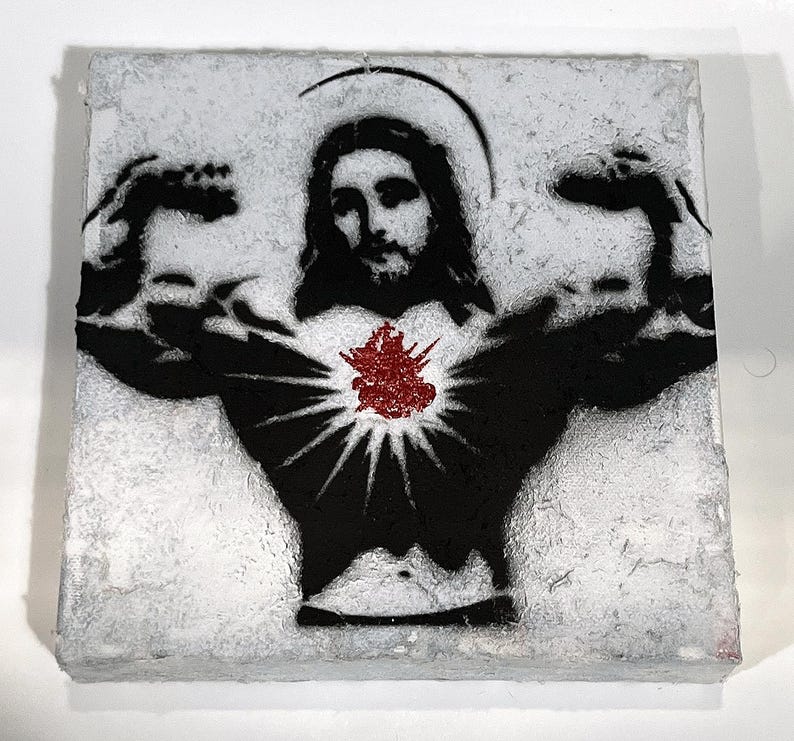 May include: A square, textured art piece featuring a black and white stencil of Jesus flexing his arms. A red, textured heart is in the center of his chest. A halo is above his head. The art piece has a white, textured background.