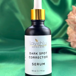 May include: A black skincare serum bottle with a white label featuring the text "Lavishly Skincare Dark Spot Corrector Serum". The bottle has a gold-colored dropper and a white tip. The bottle contains 50 ml / 1.7 fl oz of serum.