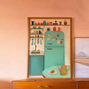 Peut inclure: Illustration encadrée d'une cuisine rétro avec un réfrigérateur turquoise, des étagères avec des tasses colorées et une théière. L'œuvre est placée contre un mur pêche, avec une commode en bois au premier plan.