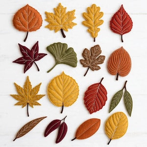 May include: A collection of felt leaves in various shapes and autumn colors including orange, yellow, red, brown, and green. Each leaf features decorative white stitched veins and a small brown stem, arranged in a grid pattern on a white surface.