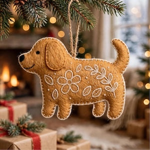May include: A tan felt dog ornament featuring white embroidered floral and leaf patterns on its side. The dog has a black stitched nose and eye, with a jute twine loop at the top for hanging. The edges are finished with white blanket stitching.