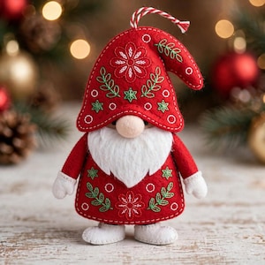 May include: A red felt gnome ornament featuring a tall, pointed hat with white and green floral embroidery, a large beige nose, a thick white beard, white mittens, and white boots. A red and white twisted string is attached to the top of the hat.