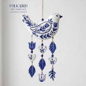 May include: A white ceramic bird ornament featuring blue floral patterns, suspended by a string. Three vertical strands hang from the bird, decorated with blue and white ceramic shapes including hearts, leaves, and tulips. Text reads FOLK BIRD.