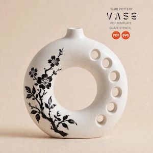 May include: A white donut-shaped ceramic vase featuring a black floral branch illustration on the left side and a vertical row of six circular cutouts on the right. Text at the top reads SLAB POTTERY VASE PDF TEMPLATE GLAZE STENCIL.