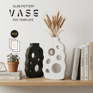 May include: Two ceramic vases, one black and one white, with circular cutouts. The white vase contains wheat. The text reads "SLAB POTTERY VASE PDF TEMPLATE". The vases sit on a wooden shelf with books and a small plant.