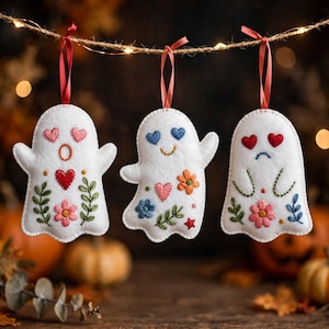 May include: Three white felt ghost ornaments hanging from a string. Each ghost features hand-stitched embroidery including hearts, flowers, and leaves in red, pink, blue, orange, and green. Each ornament is suspended by a thin red ribbon.