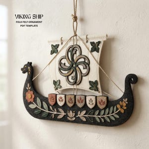 May include: A dark grey felt Viking ship ornament featuring a cream-coloured sail with a dark green and brown knotwork design. The ship hull is decorated with embroidered floral vines and six small shields. Text reads: VIKING SHIP FOLK FELT ORNAMENT PDF TEMPLATE.