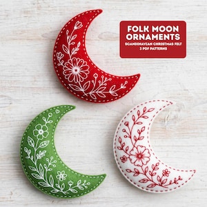 May include: Three crescent moon ornaments in red, green, and white felt, each featuring white or red floral embroidery. The text FOLK MOON ORNAMENTS SCANDINAVIAN CHRISTMAS FELT 3 PDF PATTERNS is displayed in a red box in the upper right corner.