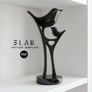 Op de afbeelding: Een glanzend zwarte keramische sculptuur van twee vogels die op een gestileerde tak zitten. De sculptuur heeft een glad, reflecterend oppervlak en staat op een ronde basis. De tekst "SLAB POTTERY TEMPLATE PDF" is zichtbaar.
