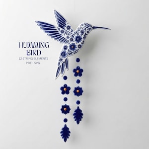 May include: A white hummingbird wall hanging with blue floral patterns and gold accents. Two vertical strings hang from the bird, featuring blue flower and leaf shapes with gold centers. Text reads: HUMMING BIRD 12 STRING ELEMENTS PDF - SVG.