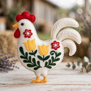 May include: A white felt rooster ornament featuring a red comb and wattle, yellow beak, and orange feet. The body is decorated with two yellow tulip appliques, green embroidered leaves, and two red flower appliques with white stitched centers.