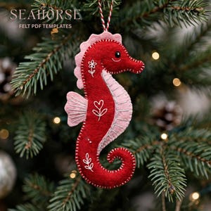 May include: A red and light pink felt seahorse ornament featuring white embroidered floral and heart details, a black bead eye, and a red and white twisted string hanger. The text SEAHORSE FELT PDF TEMPLATES is visible in the upper left corner.