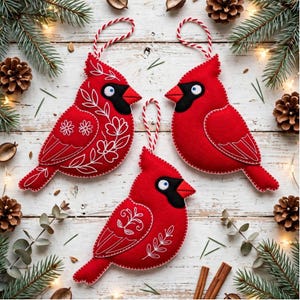 May include: Three red felt cardinal bird ornaments with white stitched floral patterns and black face masks. Each bird features a white hanging loop made of red and white twisted cord, designed for display as seasonal hanging decorations.