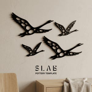 May include: Four black metal swan wall decorations with openwork designs are mounted on a light-colored wall. The swans are in various stages of flight. The text "SLAB POTTERY TEMPLATE" is below the swans.