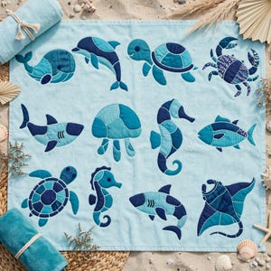 May include: A light blue rectangular towel featuring a patchwork-style appliqué design of various sea creatures including a whale, dolphin, sea turtle, crab, shark, jellyfish, seahorse, fish, and manta ray in shades of blue and teal.