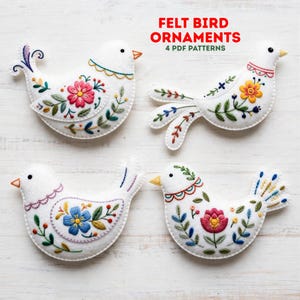 May include: Four white felt bird ornaments featuring colorful floral embroidery patterns. Each bird has a small orange beak and intricate stitching in shades of pink, blue, yellow, and green. The text FELT BIRD ORNAMENTS 4 PDF PATTERNS is visible.