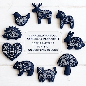 May include: A set of dark blue felt ornaments featuring white embroidered floral and folk-inspired designs of a reindeer, bird, horse, hedgehog, heart, rabbit, mushroom, bear, and cat, with text reading SCANDINAVIAN FOLK CHRISTMAS ORNAMENTS.