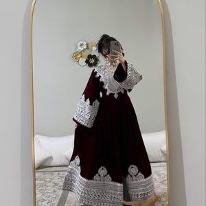 May include: A long, burgundy dress with detailed white lace trim on the sleeves and hem. The dress features a high neckline and wide sleeves. The image is reflected in a mirror.