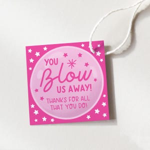 May include: A square, hot pink gift tag with white stars around the border. The tag features the words "YOU BLOW US AWAY! THANKS FOR ALL THAT YOU DO!" in pink script and a bubble design.