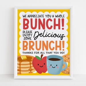 May include: A framed print with a yellow background and the words "WE APPRECIATE YOU A WHOLE BUNCH! PLEASE ENJOY SOME Delicious BRUNCH! THANKS FOR ALL THAT YOU DO!" in red and black. The image includes illustrations of pancakes, an apple, a coffee cup, and a bagel.