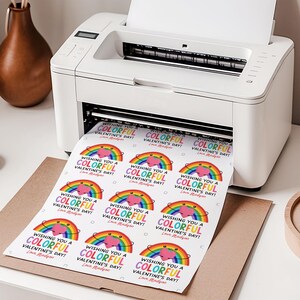 May include: A white printer printing Valentine's Day stickers. Each sticker features a rainbow, heart, and the text "Wishing You a Colorful Valentine's Day!" in various colors. The printer is on a white surface.