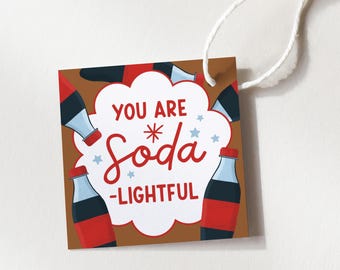 May include: A brown gift tag with the words "YOU ARE * Soda -LIGHTFUL" in red and white. The tag features illustrations of soda bottles with red caps and blue bottles. A white string is attached.