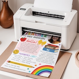 May include: A white desktop printer outputting a printed teacher introduction sheet. The document features the text 'TEACHER MRS. ANDERSON', a photo of a person, a red apple, a yellow bow, a stack of books, a smiley face, and a rainbow graphic.