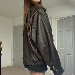 May include: A brown leather jacket with a bomber design. It has a ribbed hem and cuffs, a zip-up front, and a classic collar. The leather has a distressed appearance, giving it a vintage feel. The jacket is a medium size.
