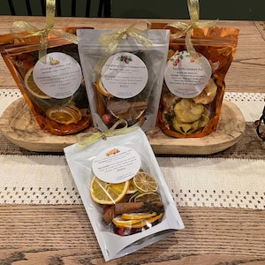 May include: An assortment of simmer pot sachets in clear and orange cellophane bags, tied with gold ribbons. The sachets contain dried fruit and spices. The labels read "Orange Simmer Pot", "Christmas Spice Simmer Pot", and "Apple Pie Simmer Pot".
