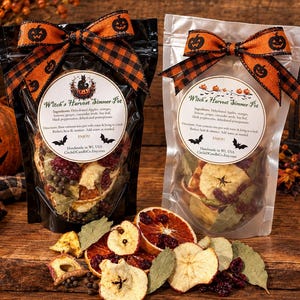 May include: Two clear pouches of Witch's Harvest Simmer Pot ingredients, each topped with an orange and black pumpkin-patterned bow. The labels list ingredients like dehydrated apples, oranges, and spices, with instructions to simmer in water.