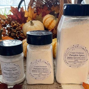 May include: Three clear plastic containers of Pumpkin Spice carpet freshener with black lids, labeled with ingredients and sizes of 5oz, 9oz, and 16oz. The containers are filled with a fine, off-white powder and feature circular white labels.