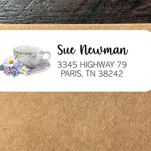 May include: White return address label with a floral design featuring a teacup and daisies. The text reads "Sue Newman, 3345 HIGHWAY 79, PARIS, TN 38242".