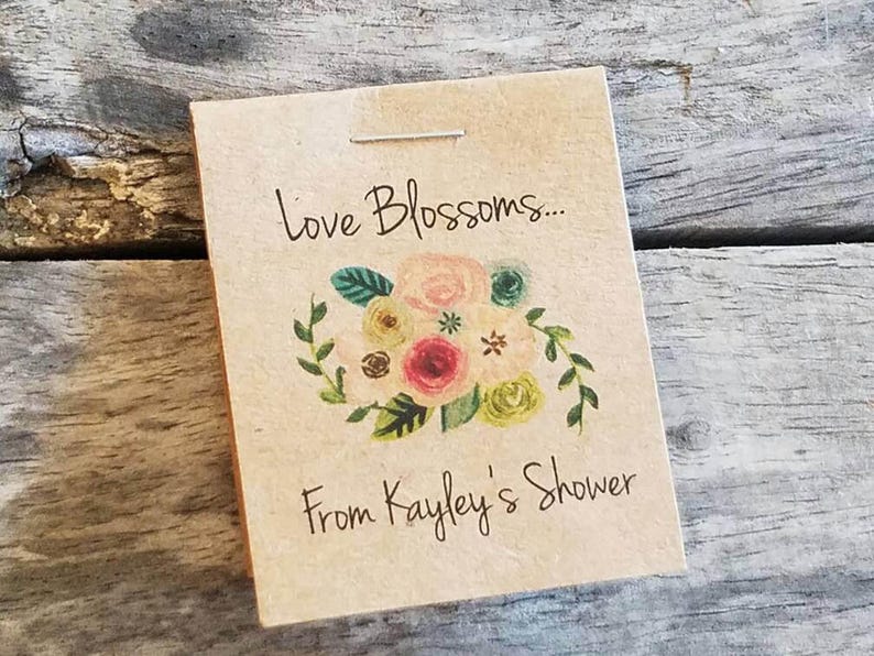Pu&ograve; includere: Un biglietto marrone con il testo "Love Blossoms... From Kayley's Shower" e un'illustrazione floreale con fiori rosa, gialli e verdi.