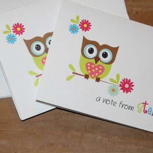 May include: White stationery cards featuring a cartoon owl with a heart-shaped belly, perched on a branch with flowers. The text "a note from stella" is written in colorful letters. Stationery set.