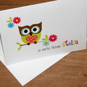 May include: White stationery card with a cartoon owl illustration. The owl is green with a brown head, large eyes, and a heart-shaped chest. The card includes the text "a note from Stella" in colorful letters, and is accompanied by a white envelope.