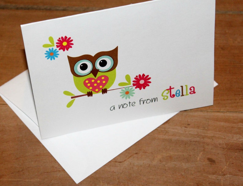 May include: White stationery card with a cartoon owl illustration. The owl is green with a brown head, large eyes, and a heart-shaped chest. The card includes the text "a note from Stella" in colorful letters, and is accompanied by a white envelope.
