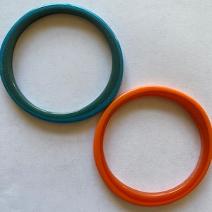 May include: Two plastic bangles, one teal blue and one orange, on a white background.