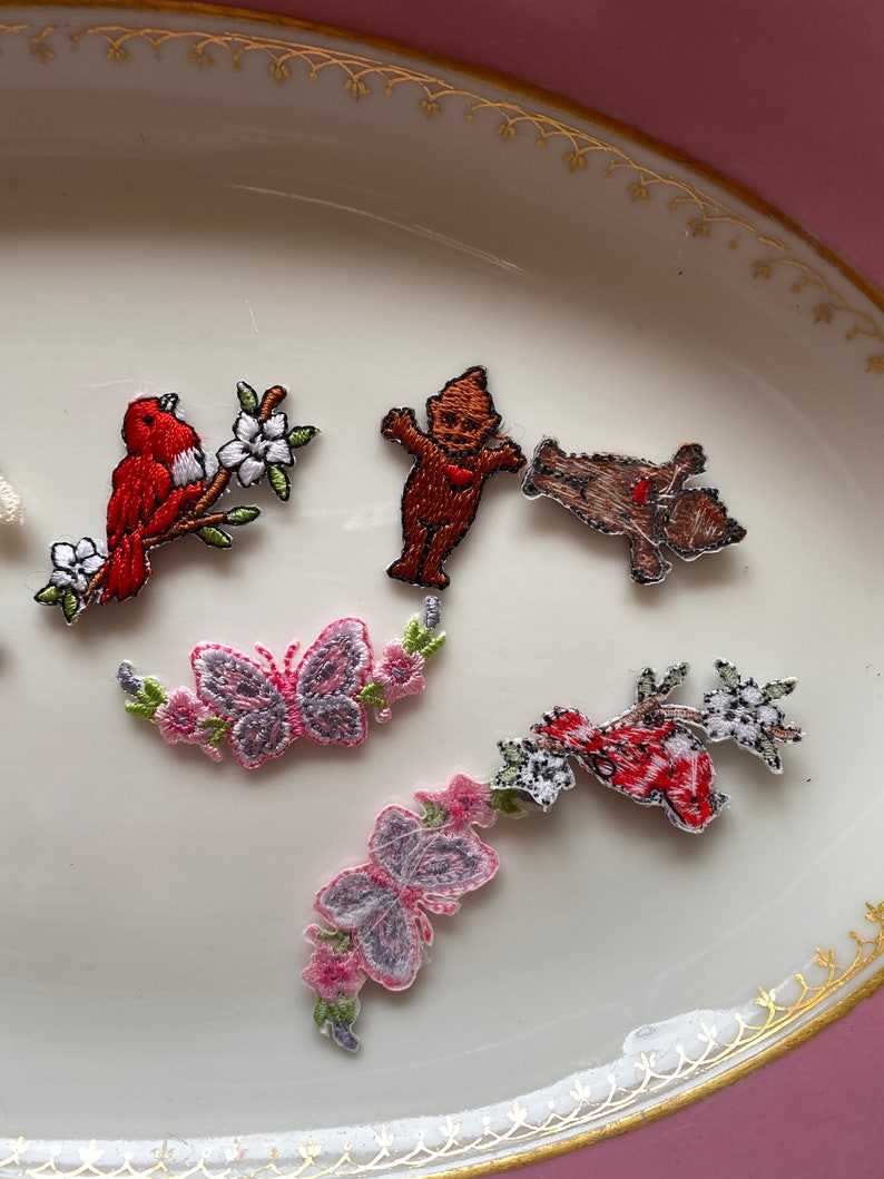 May include: Assortment of embroidered iron-on patches featuring a red bird on a branch, a butterfly, a gnome, a bear, and a red bird with white flowers.