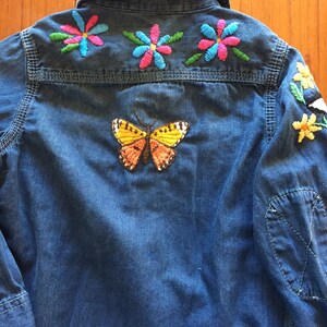 May include: A blue denim shirt with colourful embroidered flowers and a butterfly on the back.