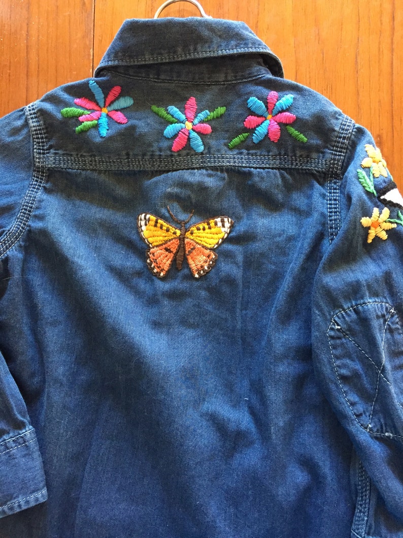 May include: A blue denim shirt with colourful embroidered flowers and a butterfly on the back.
