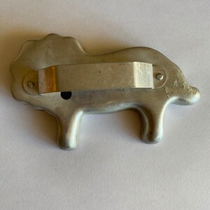 Puede incluir: Un cortador de galletas de metal plateado con forma de le&oacute;n. El cortador tiene un mango en la parte posterior.