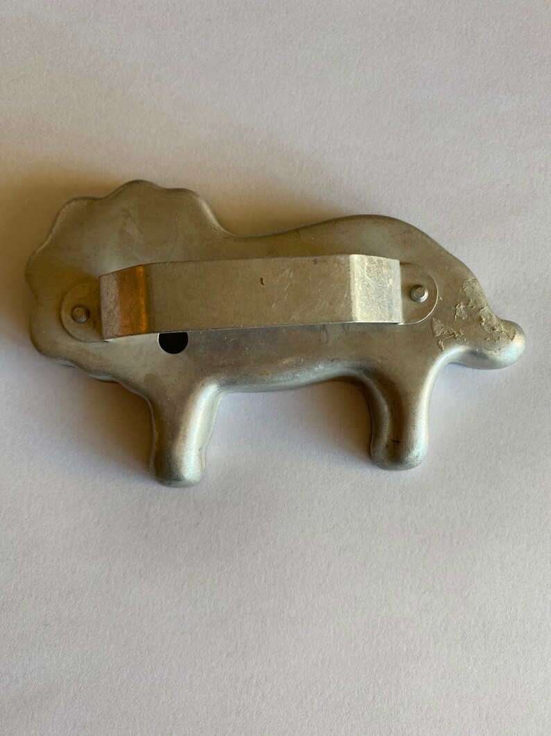 Puede incluir: Un cortador de galletas de metal plateado con forma de le&oacute;n. El cortador tiene un mango en la parte posterior.