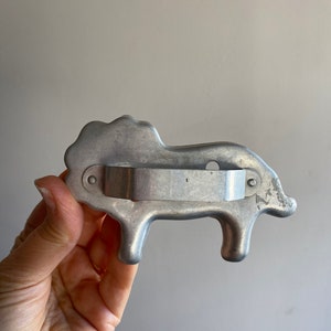 Puede incluir: Un cortador de galletas de metal plateado con forma de cerdo. El cortador tiene un mango en la parte posterior.
