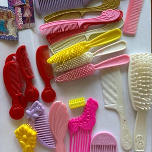 May include: A collection of vintage plastic combs in various colors, including pink, yellow, red, and purple. Some combs feature decorative designs, and there are also small Barbie and Cabbage Patch Kids cards.