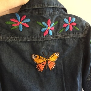 May include: A blue denim shirt with colourful embroidered flowers and a butterfly on the back.